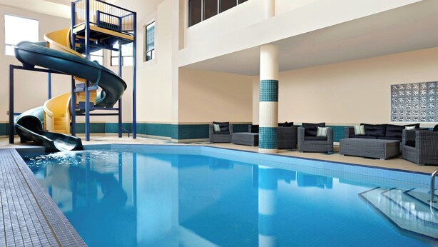Una piscina interior con un tobogán de varios niveles, un área de descanso con sofás y una pared de azulejos con un diseño.