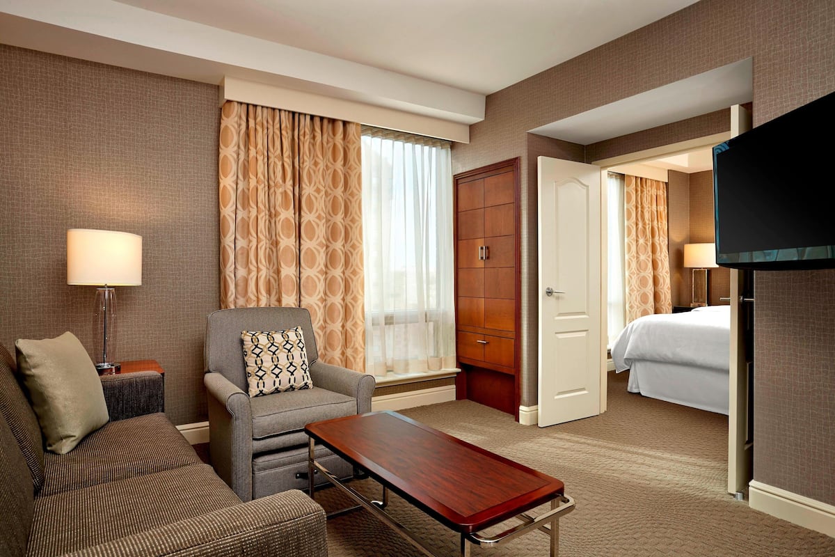 A hotel room with a sofa, armchair, wooden cabinet, and a television.