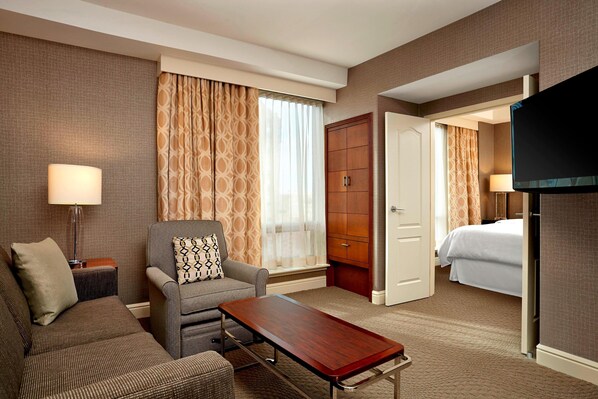 Una habitación de hotel con sofá, sillón, aparador de madera y televisor.