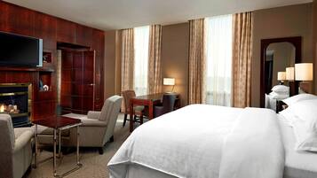 Quarto de hotel com uma cama grande, televisão, lareira, escrivaninha e uma cadeira.