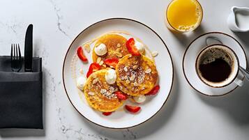 Desayuno con tortitas, fresas y una taza de café sobre una mesa de mármol.