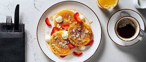 A breakfast setting with pancakes, strawberries, and a cup of coffee on a marble table.