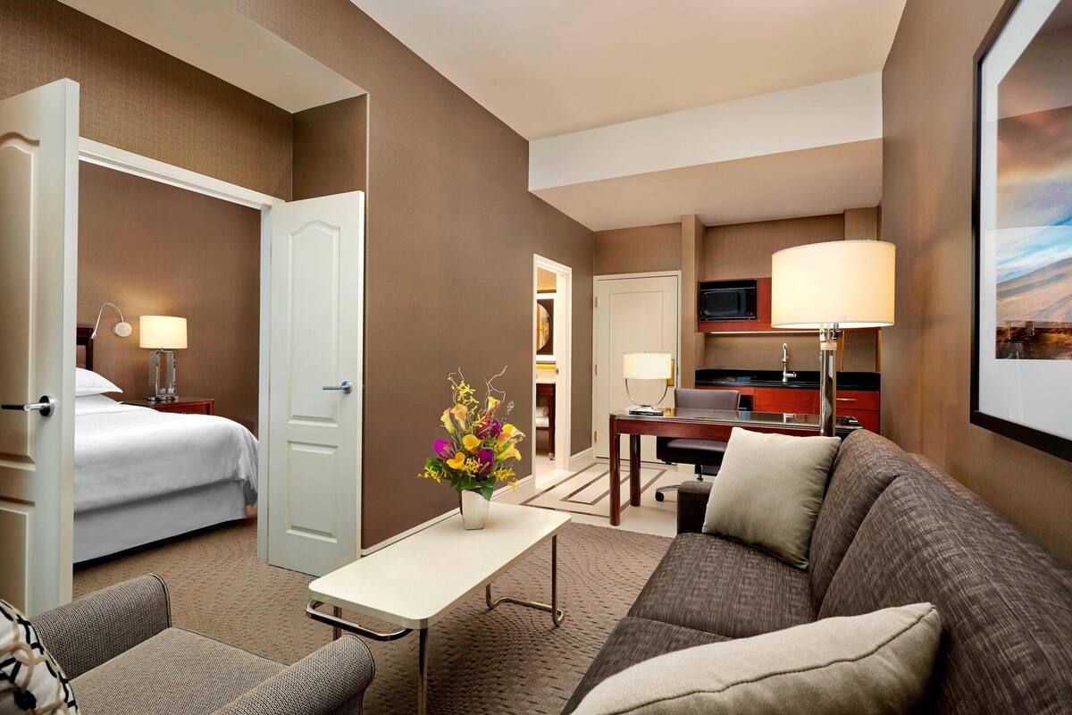 A hotel room with a bed, a sofa, a small table, a desk, and a TV.