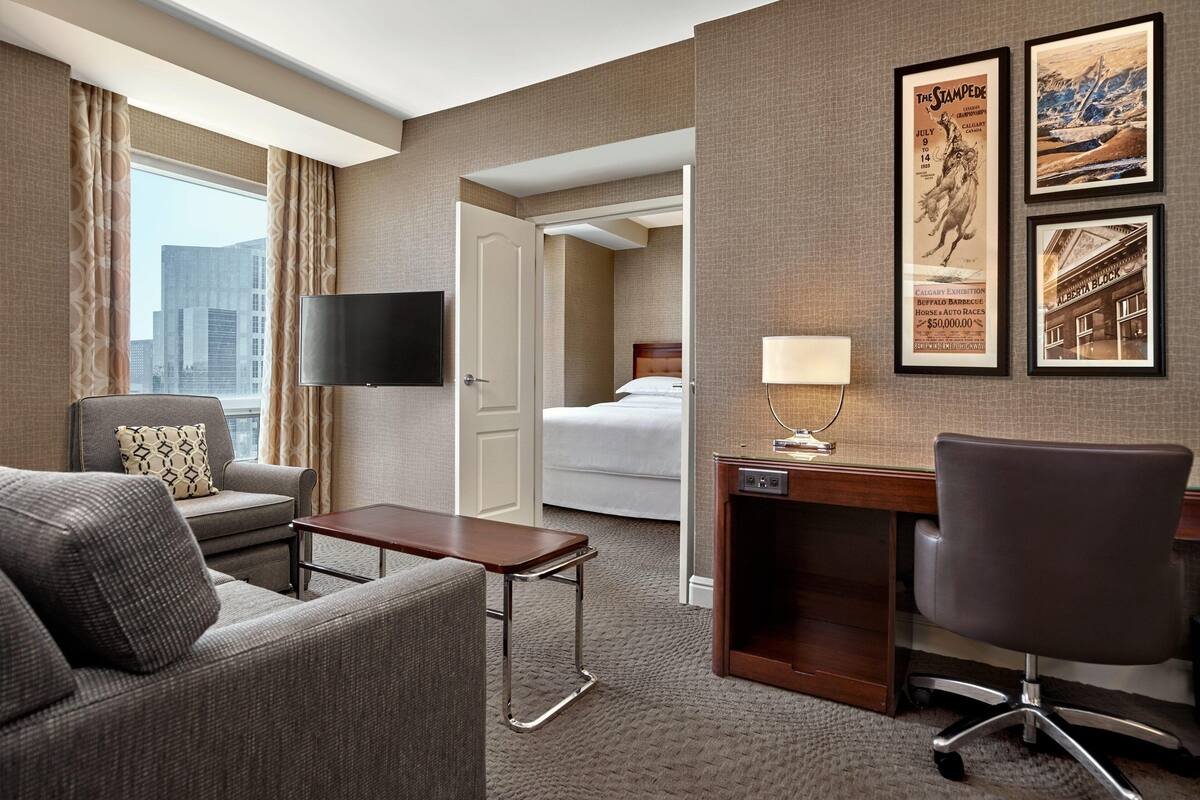 A hotel room with a sofa, a desk, a flat-screen TV, a bed, and a view of the cityscape.