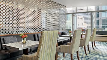 Un comedor moderno con un revestimiento de pared estampado con motivos geométricos, asientos confortables y vistas de la ciudad a través de grandes ventanales.