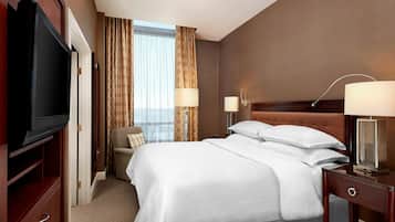Une chambre d’hôtel avec un grand lit, une télévision, un bureau avec une lampe et une vue sur la ville par la fenêtre.