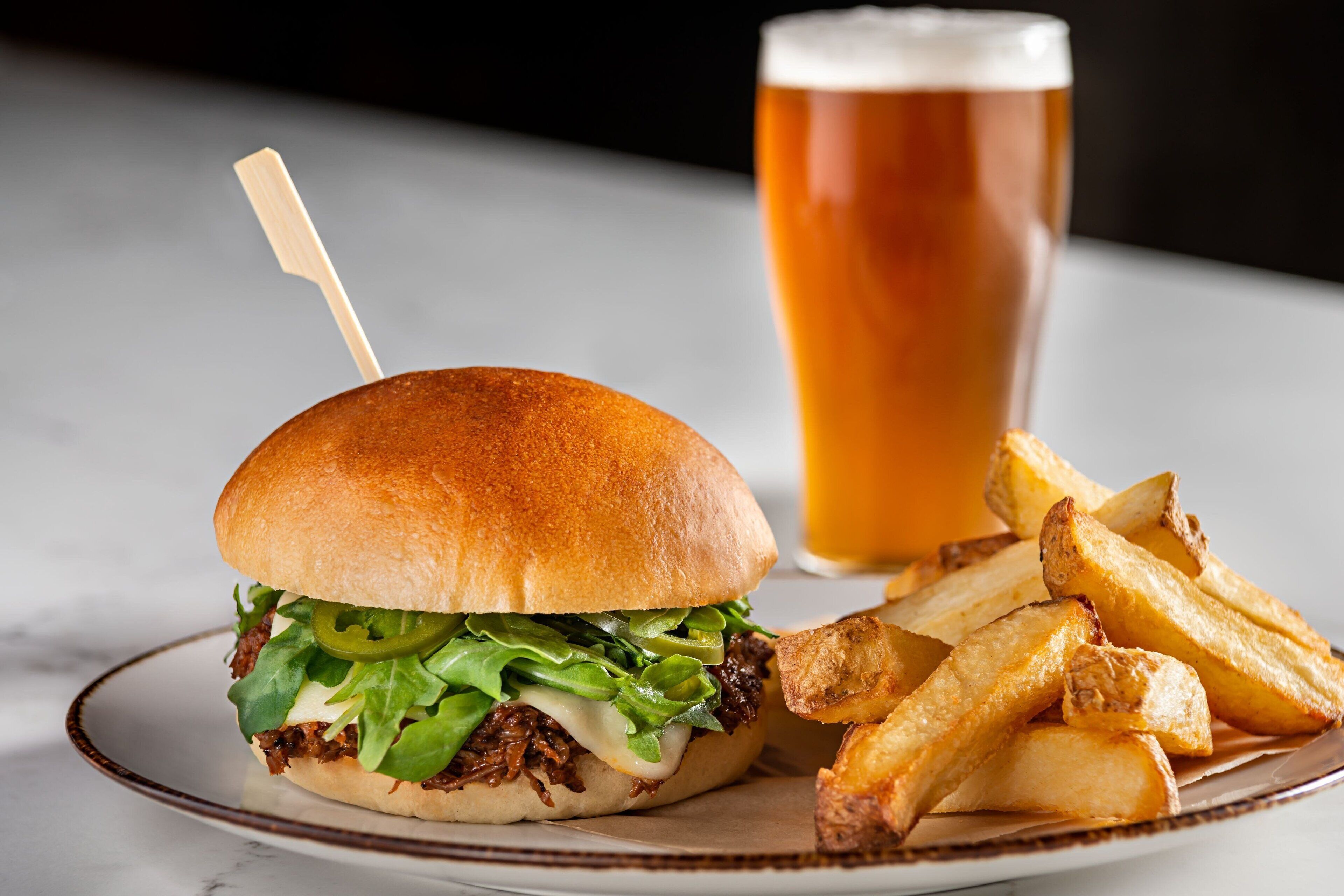 A plate with a sandwich and fries, and a glass of beer.