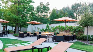 An outdoor patio area with lounge chairs, a fire pit, and umbrellas. - Courtyard by Marriott Livermore (Livermore)