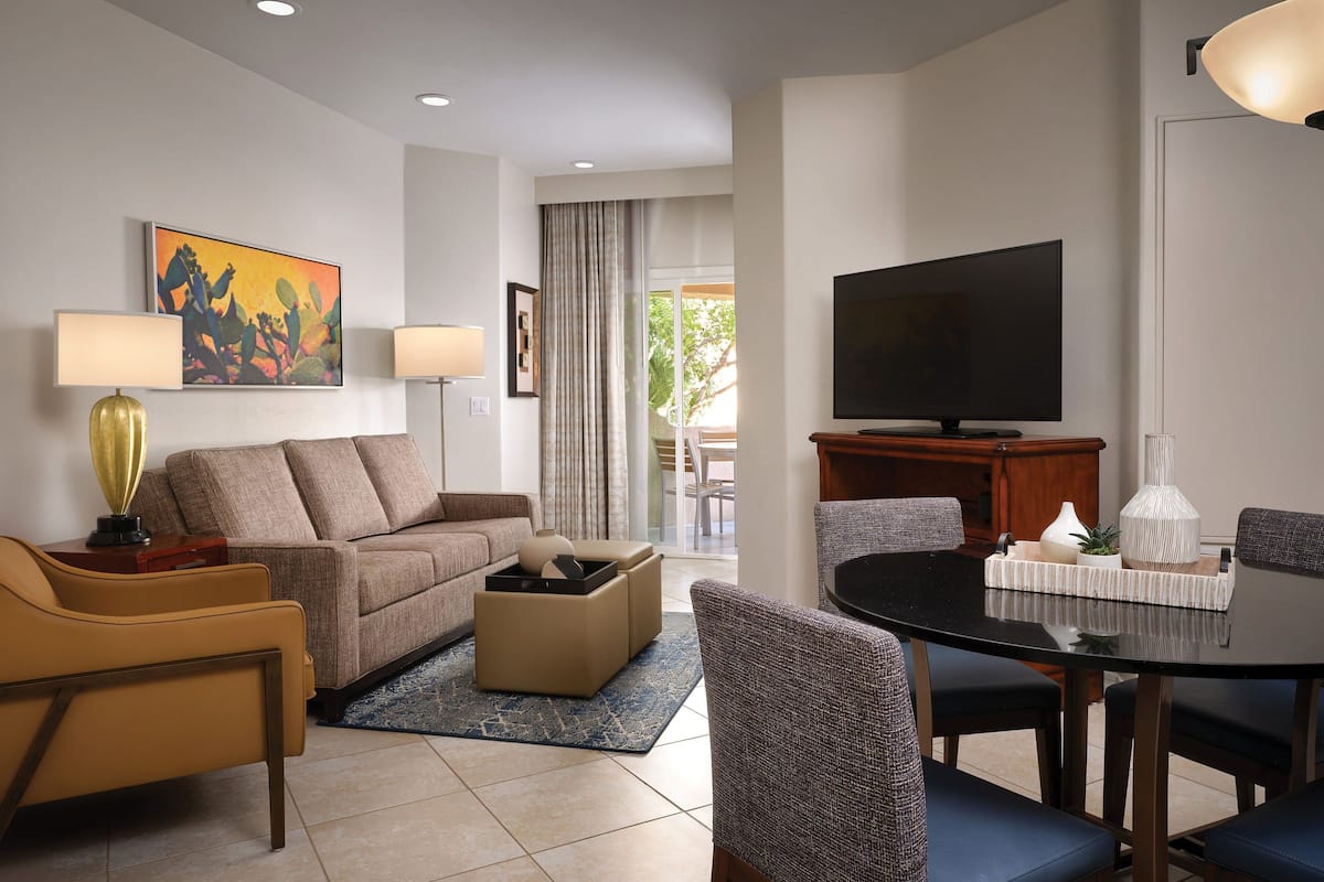 A modern living room with a sofa, armchairs, a coffee table, a dining table with chairs, a flat-screen TV, and artwork on the walls.