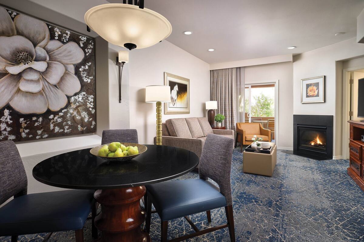 A modern living room with a round dining table, blue upholstered chairs, a sofa, and a fireplace.