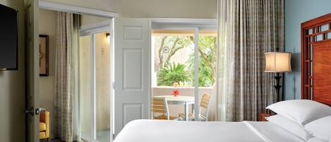 A hotel room with a bed, a table with chairs, a view of greenery outside, and a sliding door.