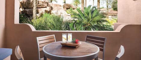 Une table ronde entourée de quatre chaises, une table en bois et une vue sur un paysage rocheux agrémenté de palmiers.