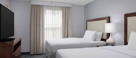 A hotel room with two beds, a ceiling fan, a TV, and a window with curtains.