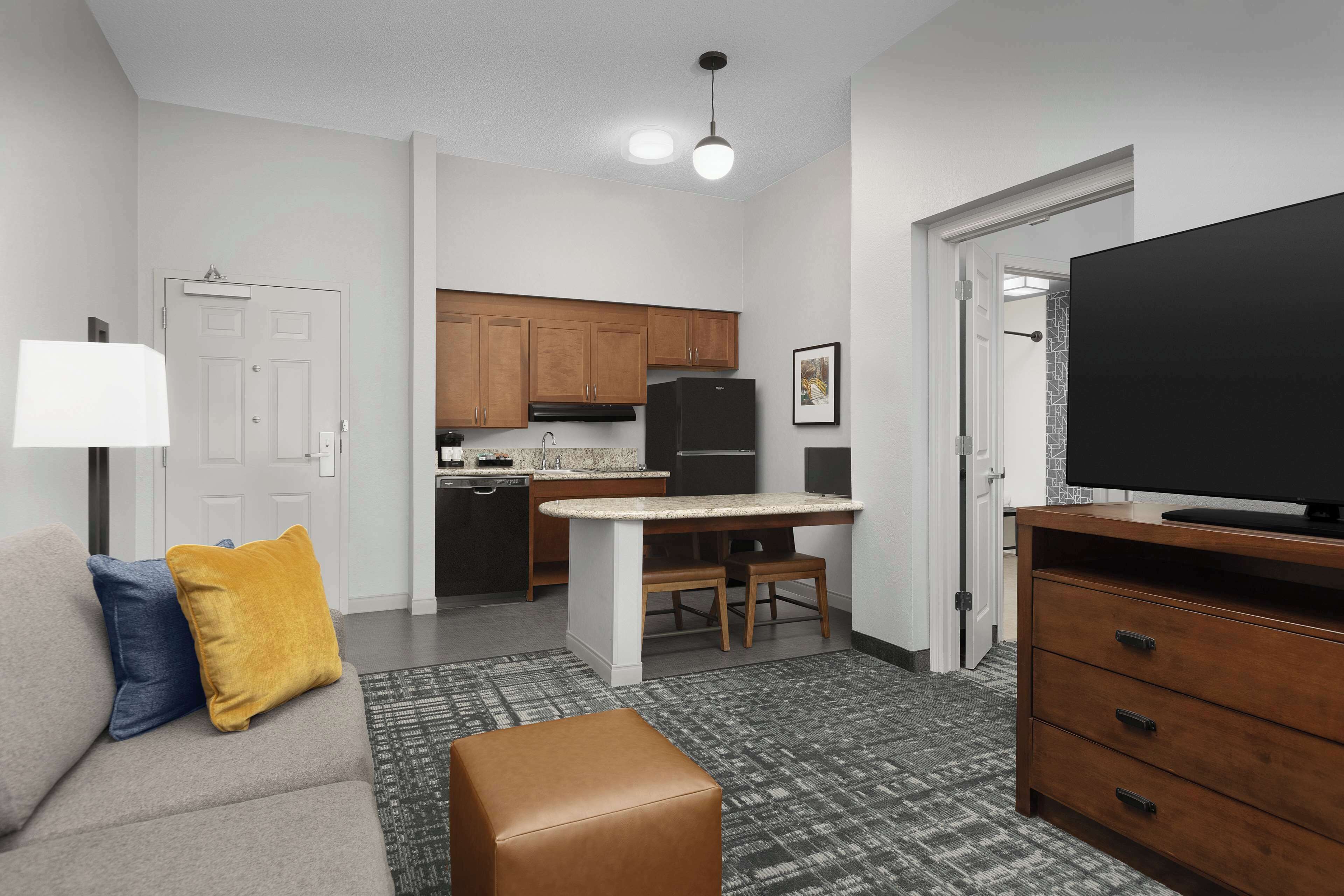 Un espacio habitable compacto con kitchenette, un sofá con cojines, un televisor y un tapete estampado.