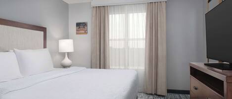 A hotel room with a bed, a desk, a television, a ceiling fan, and a window with curtains.