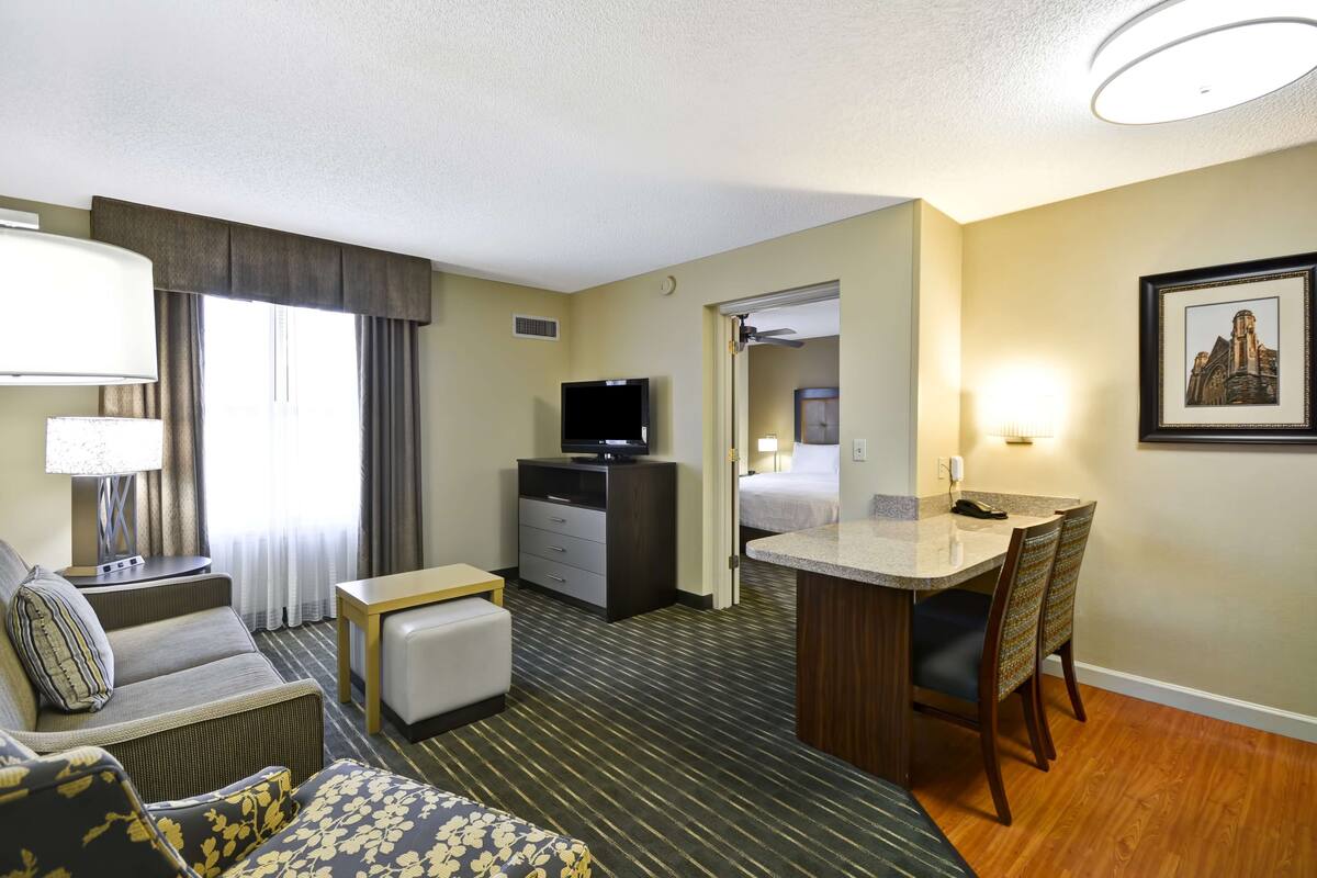 Una habitación de hotel con sofá, una mesita, un escritorio con sillas, televisión y cama.