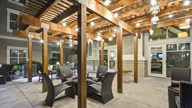 Un patio exterior con pérgolas de madera, zonas de estar y vistas del edificio contiguo.