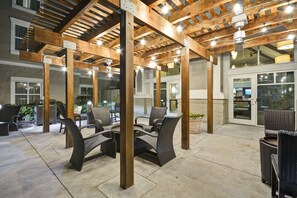 Un patio exterior con pérgolas de madera, zonas de estar y vistas del edificio contiguo.
