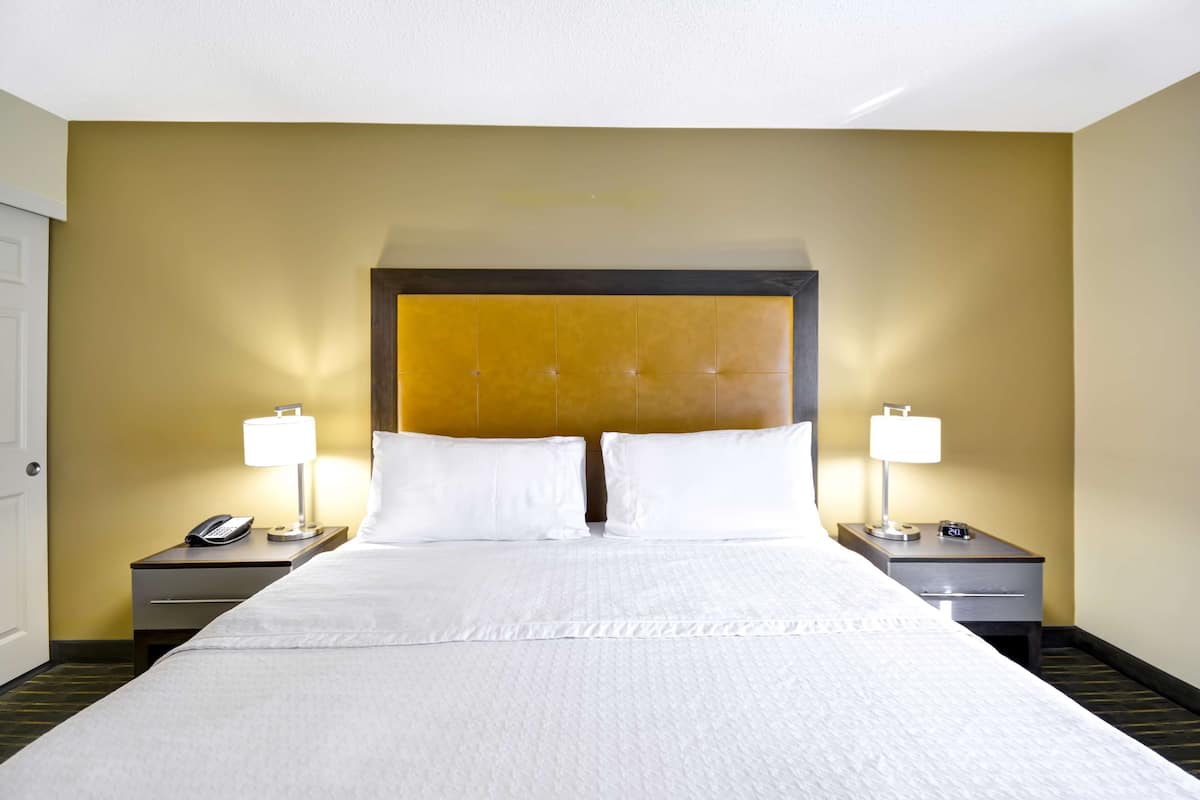 A hotel room with a large bed, two bedside tables with lamps, a telephone, and a nightstand with a clock.