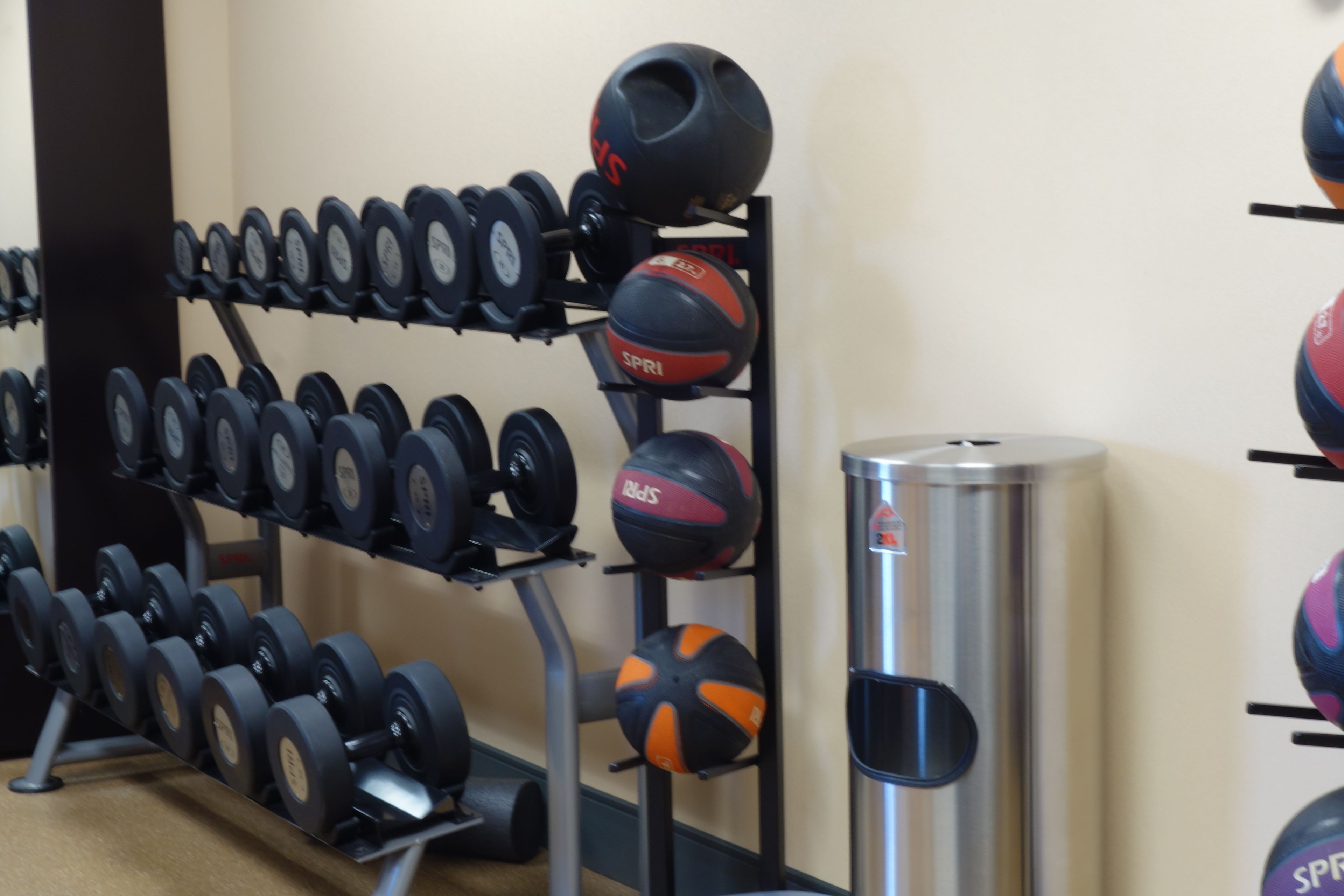 A gym with various exercise equipment including dumbbells, medicine balls, and a water bottle.