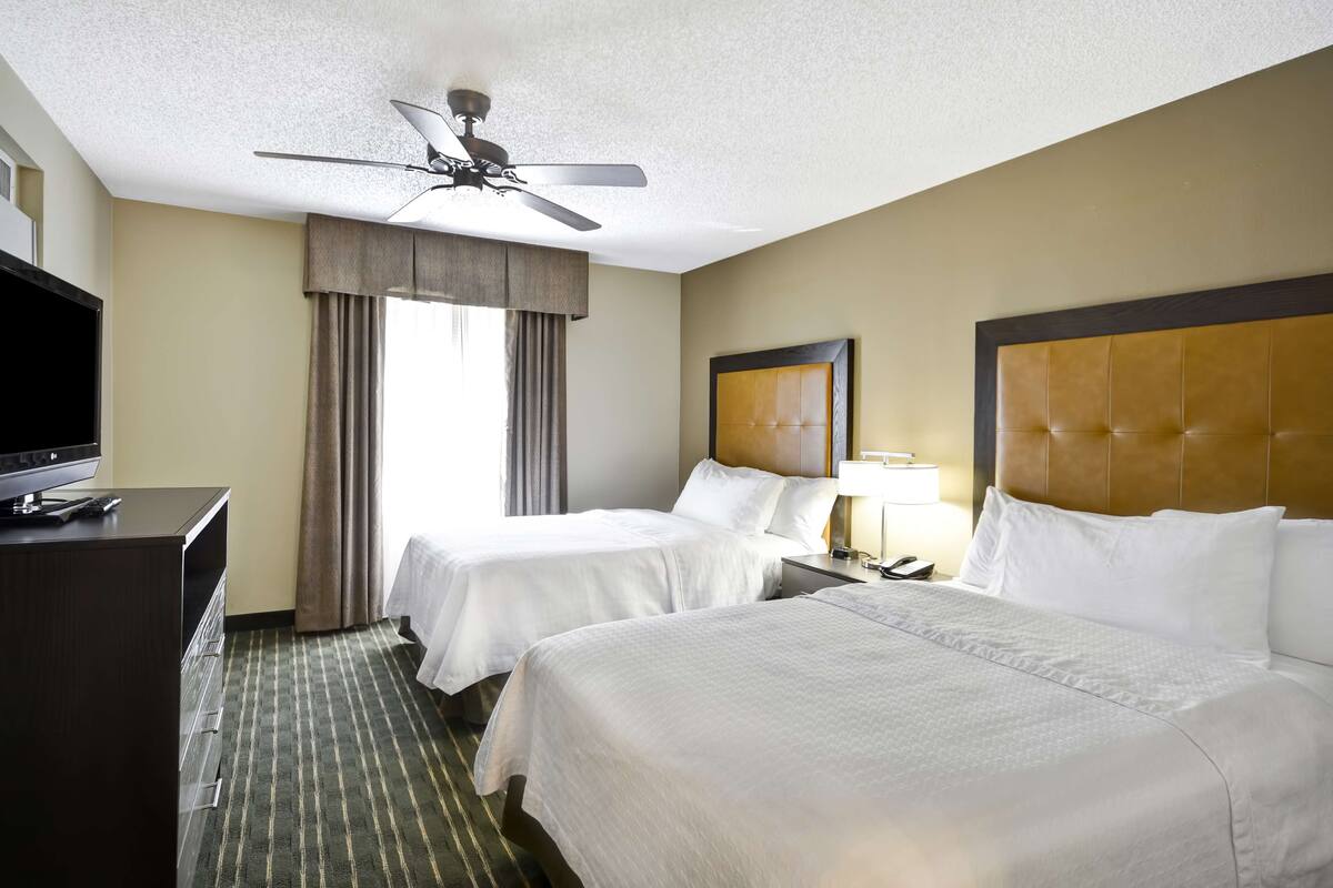 A hotel room with two beds, a ceiling fan, a TV, and a desk.