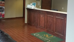 A reception area with a wooden counter, a green doormat with 'QUALITY' text, and a whiteboard on the wall. - Quality Inn & Suites Thomasville-High Point (Thomasville)