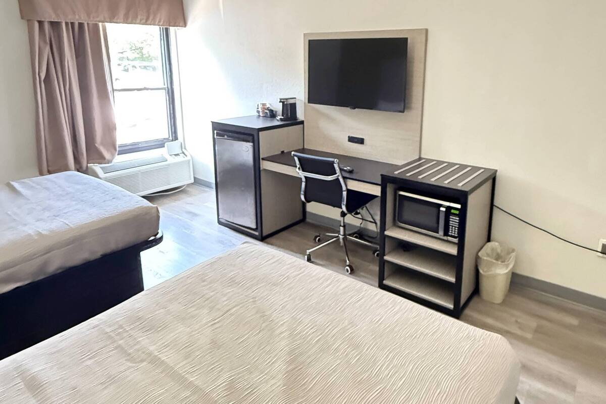 Una habitación de hotel con cama, escritorio, silla, televisión y microondas.