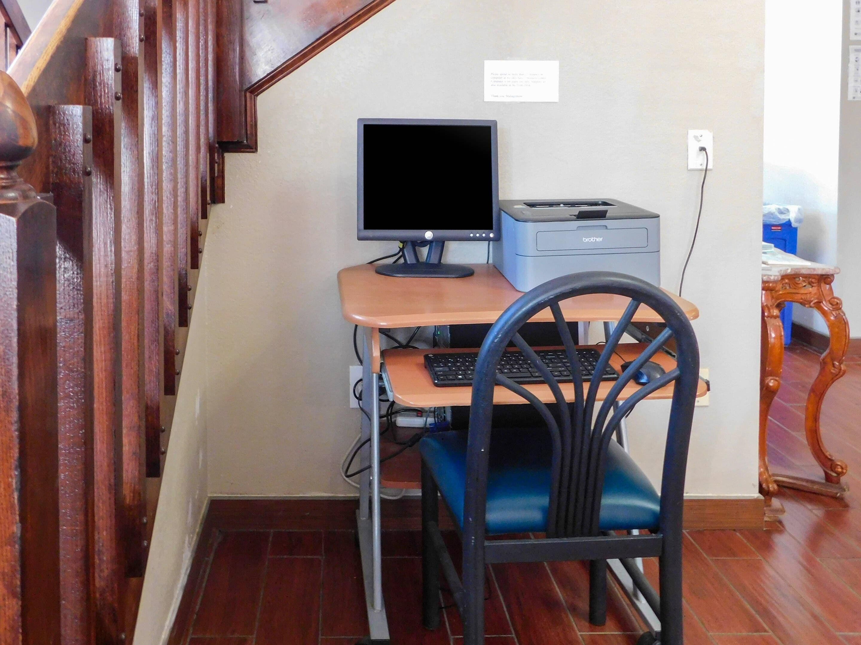 A small office space with a desk, chair, computer, printer, and a staircase.
