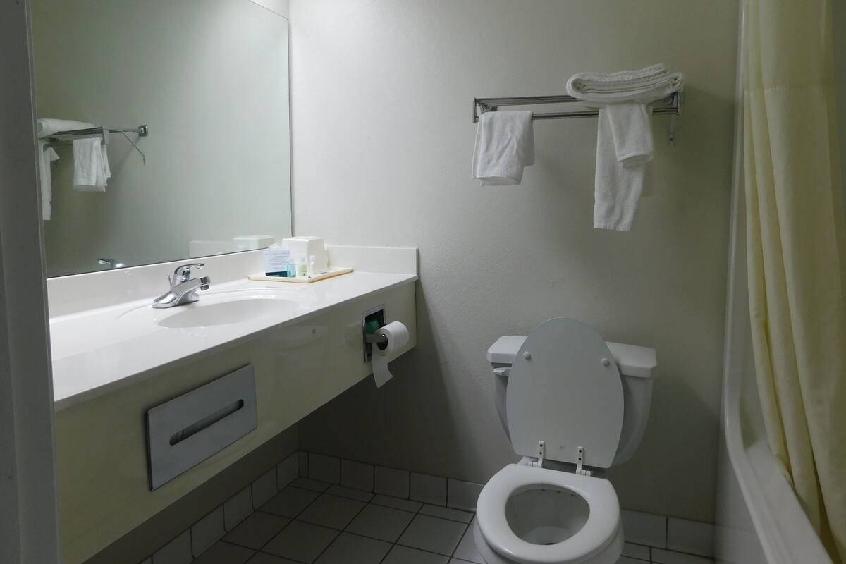 Un baño pequeño y limpio con lavamanos blanco, espejo, inodoro y toallero con toallas dobladas.