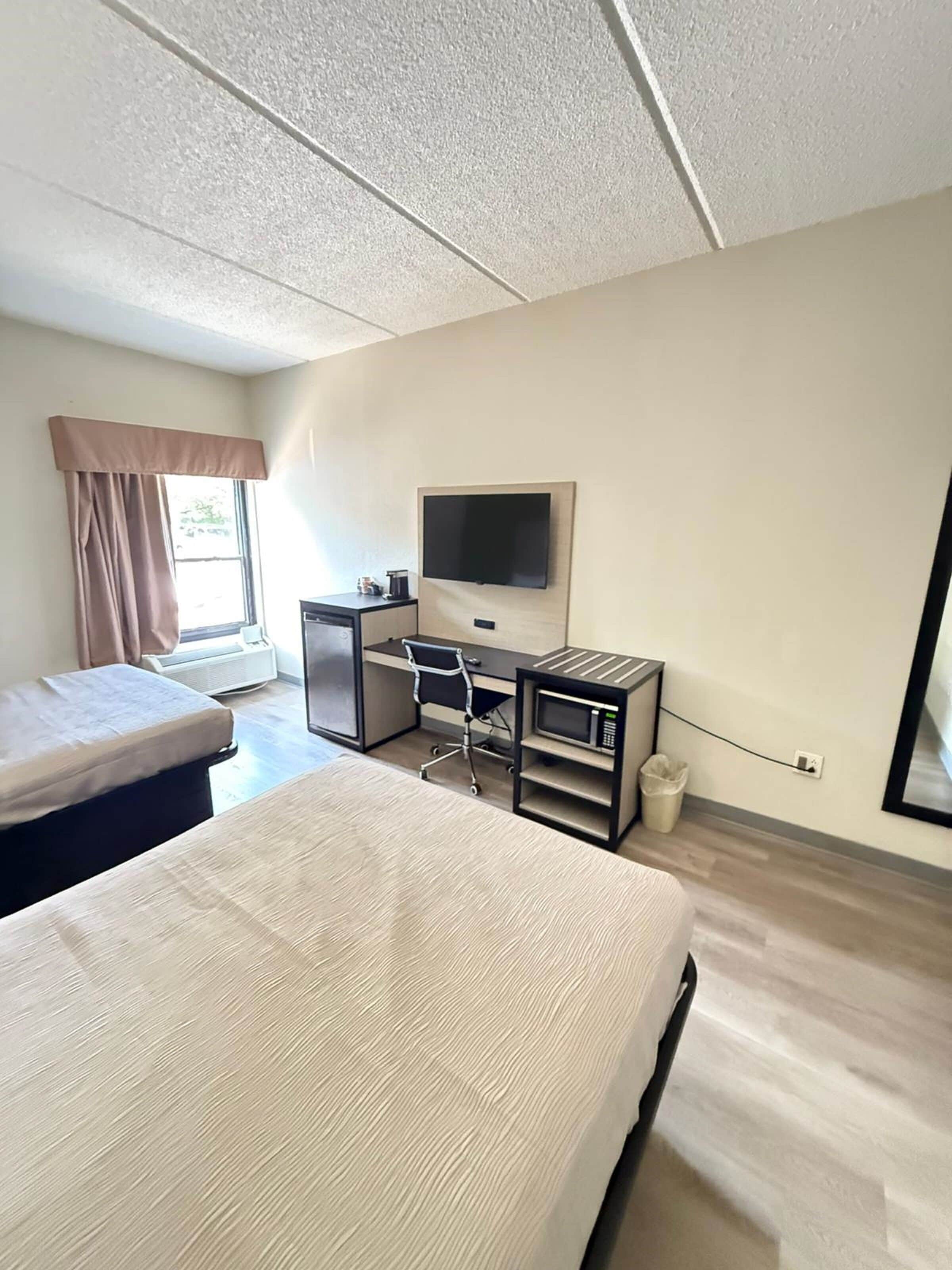 A hotel room with a bed, a desk with a chair, a television, and a window with curtains.