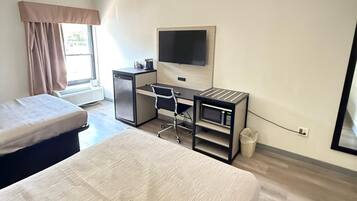 A hotel room with a bed, a desk with a chair, a television, and a window with curtains.