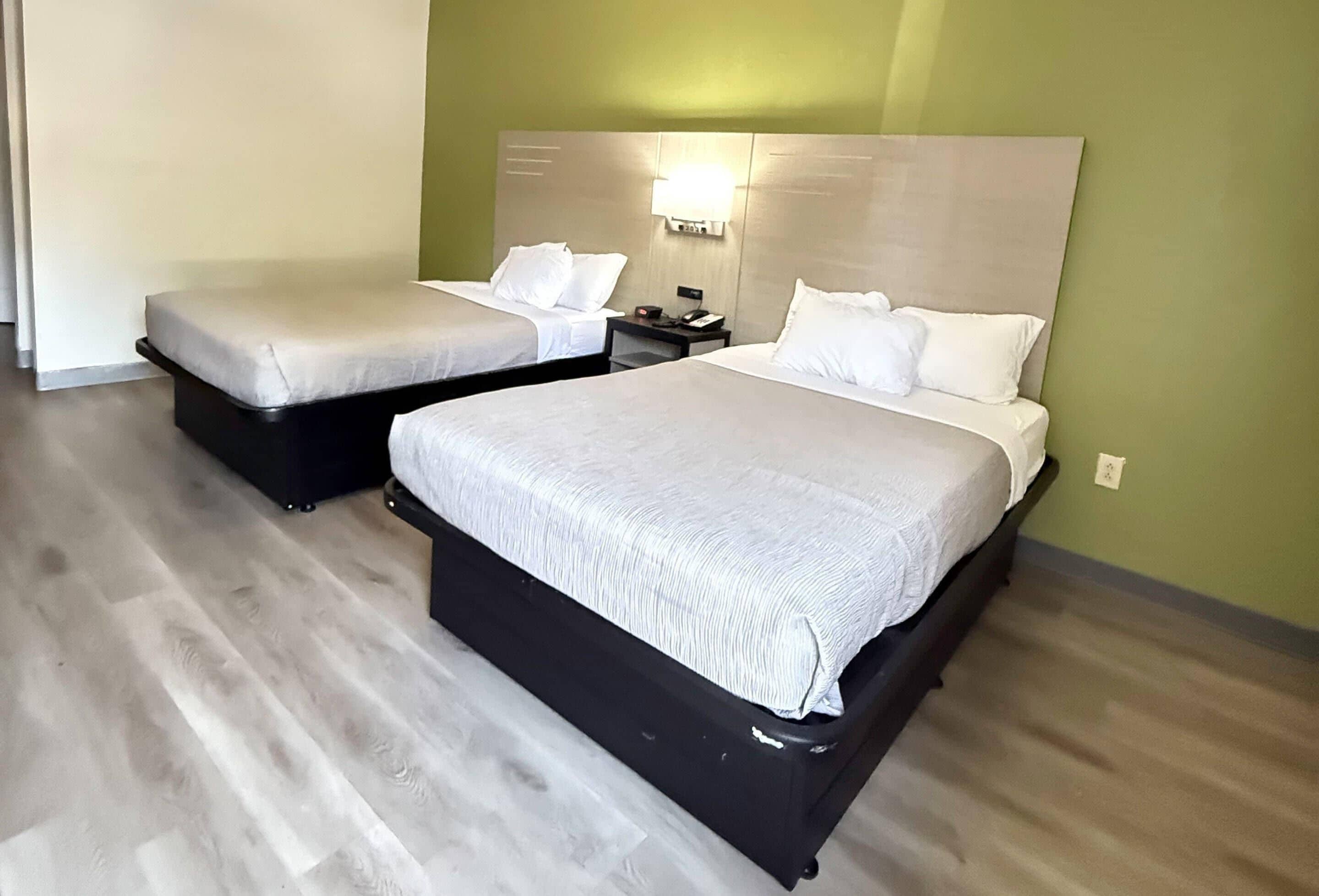 A hotel room with two beds, a nightstand, and a wall-mounted light fixture.