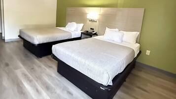 A hotel room with two beds, a nightstand, and a wall-mounted light fixture.