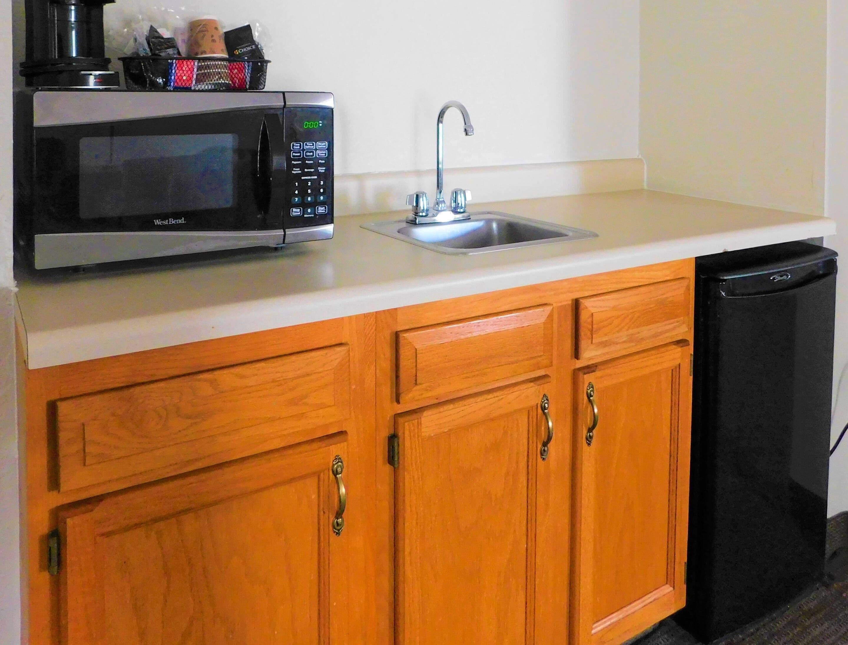 Una cocina con un microondas West Bend, un lavamanos de acero inoxidable, armarios de madera y un lavavajillas negro.