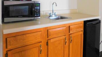 Una cocina con un microondas West Bend, un lavamanos de acero inoxidable, armarios de madera y un lavavajillas negro.