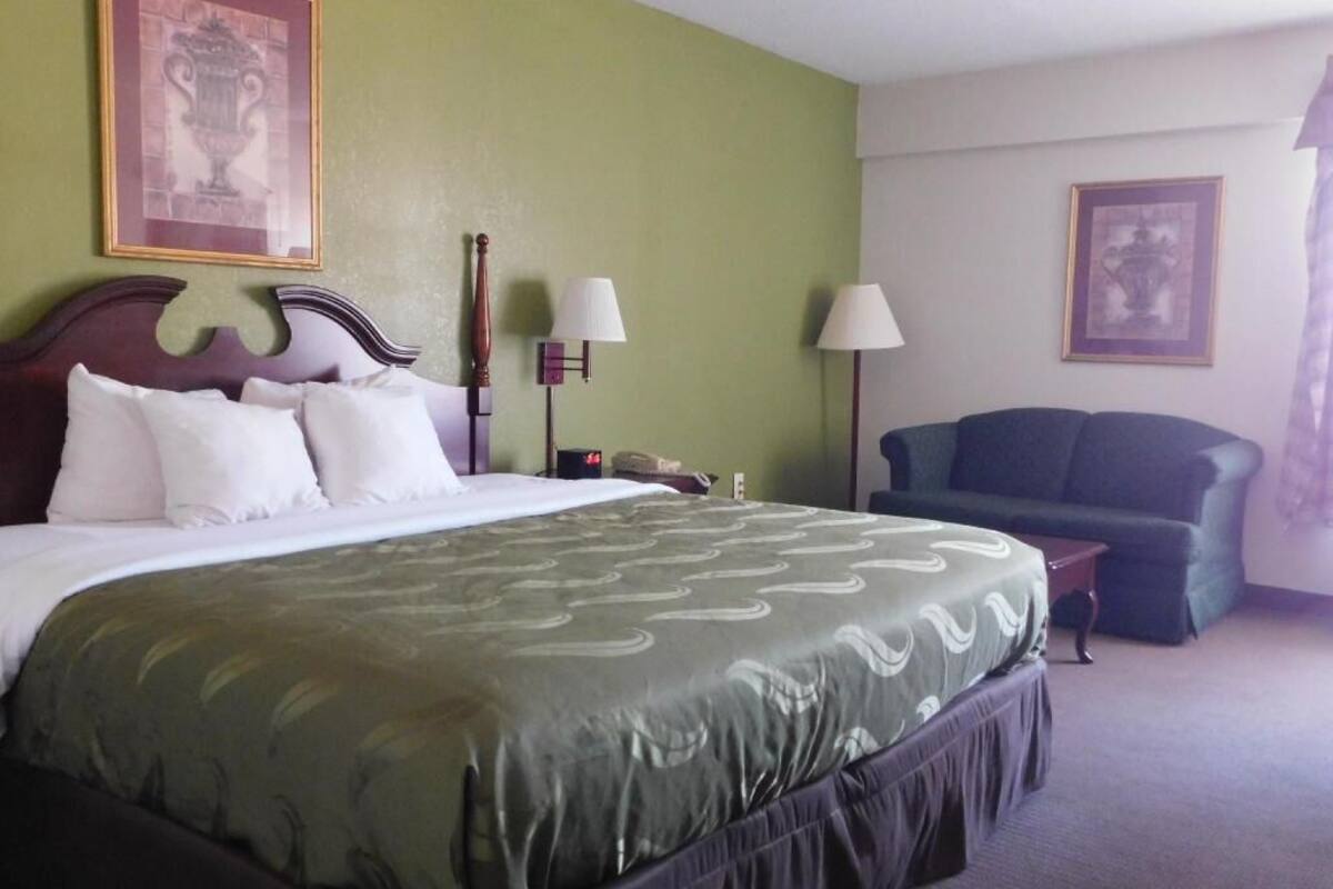 Una habitación de hotel con una cama, una silla, dos lámparas y cuadros en las paredes.