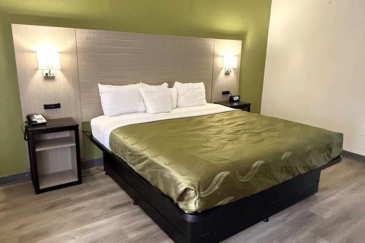 Habitación de hotel con una cama grande, dos mesitas de noche y lámparas fijadas a la pared.