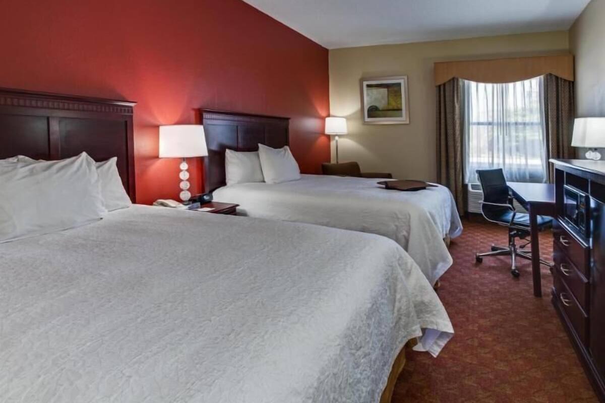 A hotel room with two beds, a desk, a chair, and a window with curtains.