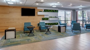 Un área de espera moderna con asientos cómodos, una televisión de pantalla plana y una pared verde con plantas.