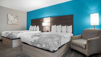 A hotel room with two beds, a chair, a nightstand, and a wall with a blue accent.