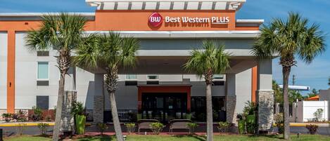 Un hotel Best Western Plus con una fachada moderna, palmeras y un cielo azul despejado.