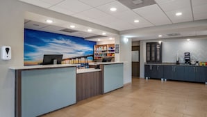 Un área de recepción con escritorio, computadora, repisa con diversos objetos y un mural en la pared.