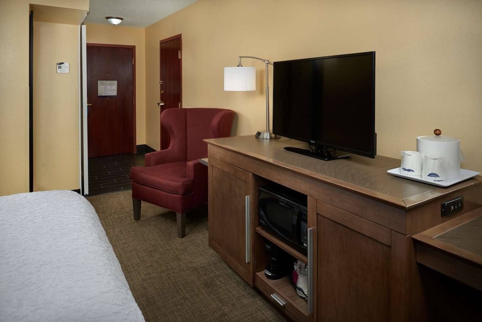 Une chambre d’hôtel avec un lit, un fauteuil rouge, une télévision, une machine à café et un petit meuble.