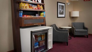 A minibar with snacks and beverages, a small table with a chair, and an exit sign on the wall. - Hampton Inn Shelbyville (Shelbyville)