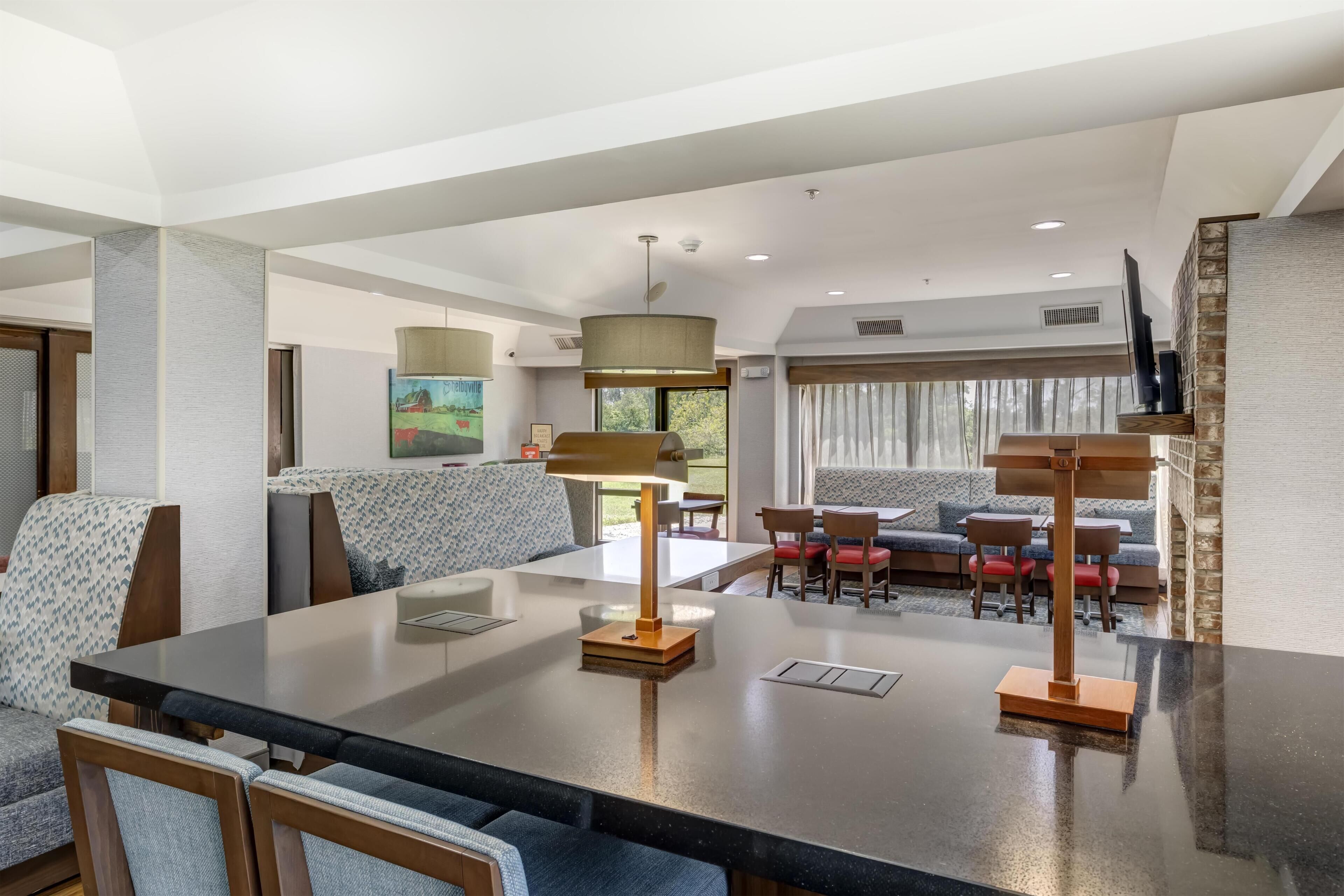 A modern hotel room with a dining area, a sofa set, and a large window.