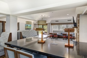 A modern hotel room with a dining area, a sofa set, and a large window.