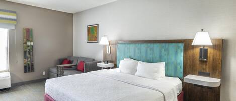 Una habitació d'hotel amb un llit gran, un sofà, una taula petita, una làmpada penjada a la paret i un quadre.