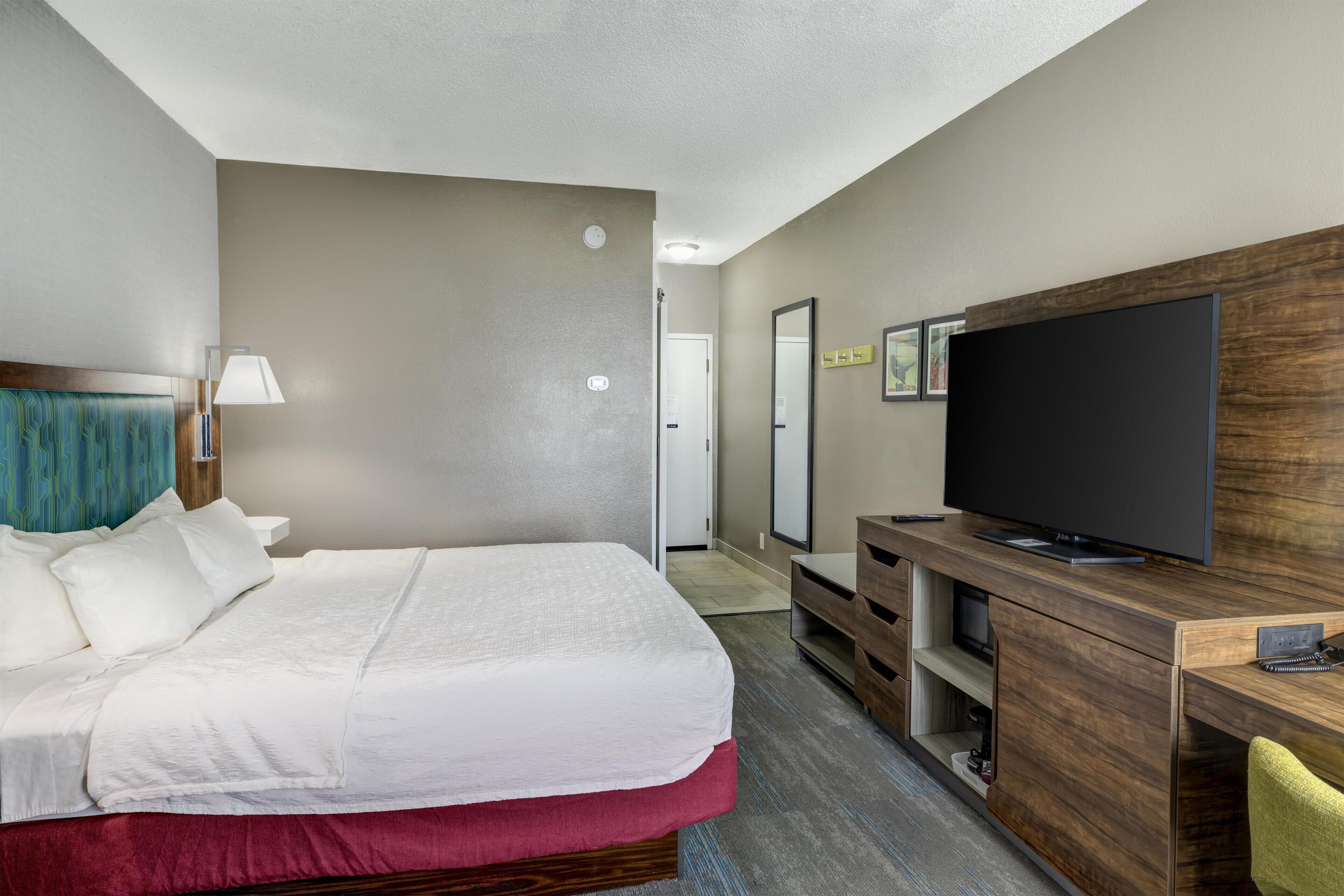 Habitación de hotel con cama, televisión, escritorio y espejo.