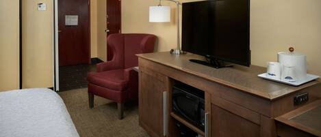 Quarto de hotel com cama, uma poltrona vermelha, televisão, máquina de café e micro-ondas.