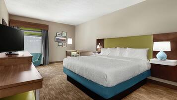 A hotel room with a large bed, a desk, a TV, and a window with curtains.